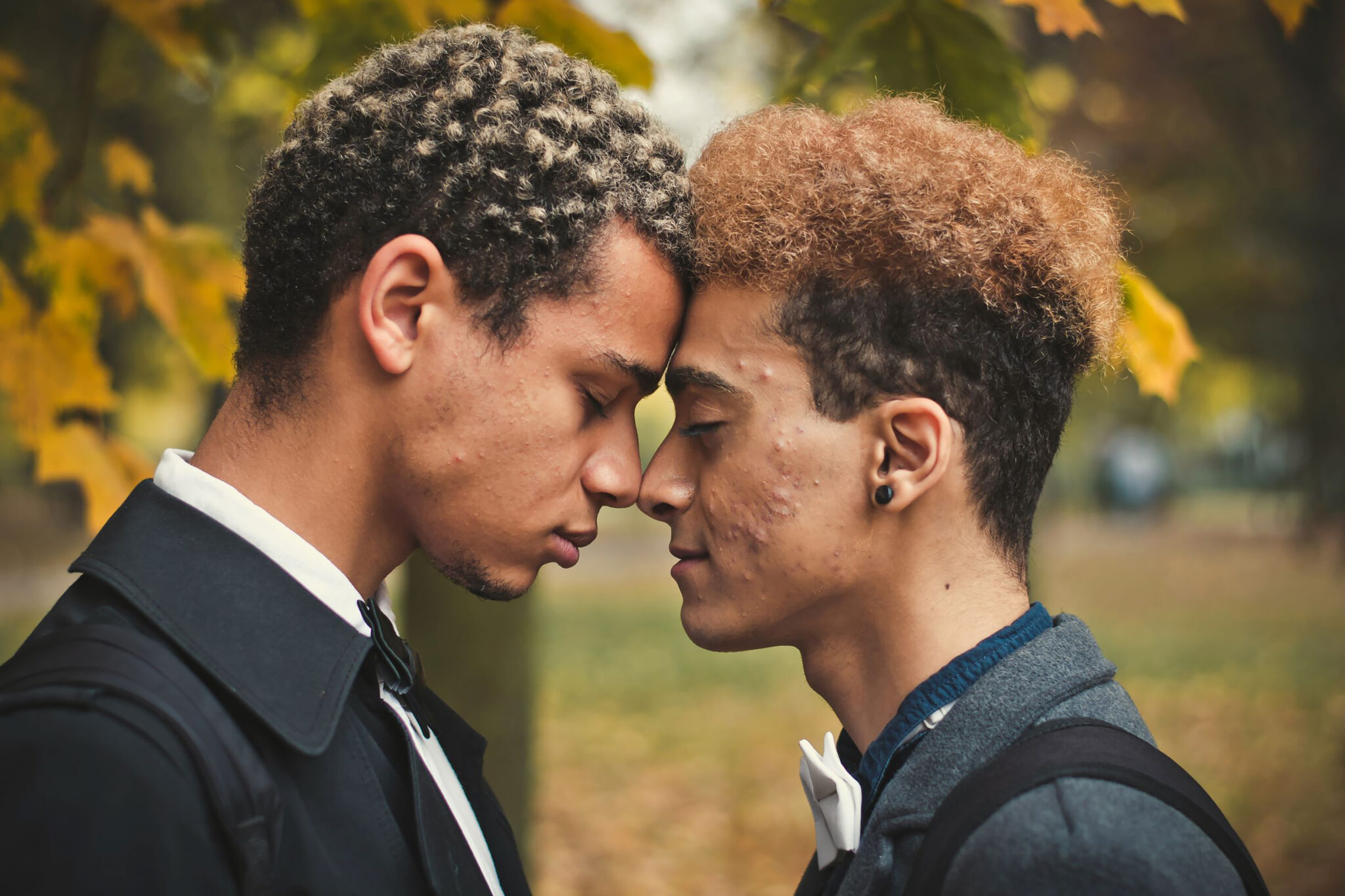 Handsome young gay couple standing head to head in park. Concept of same sex love, equality and LGBT rights